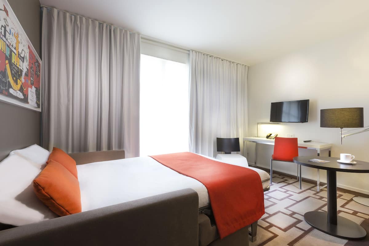 Ein Hotelzimmer mit Bett, Schreibtisch, Stuhl, Fernseher und Couchtisch.