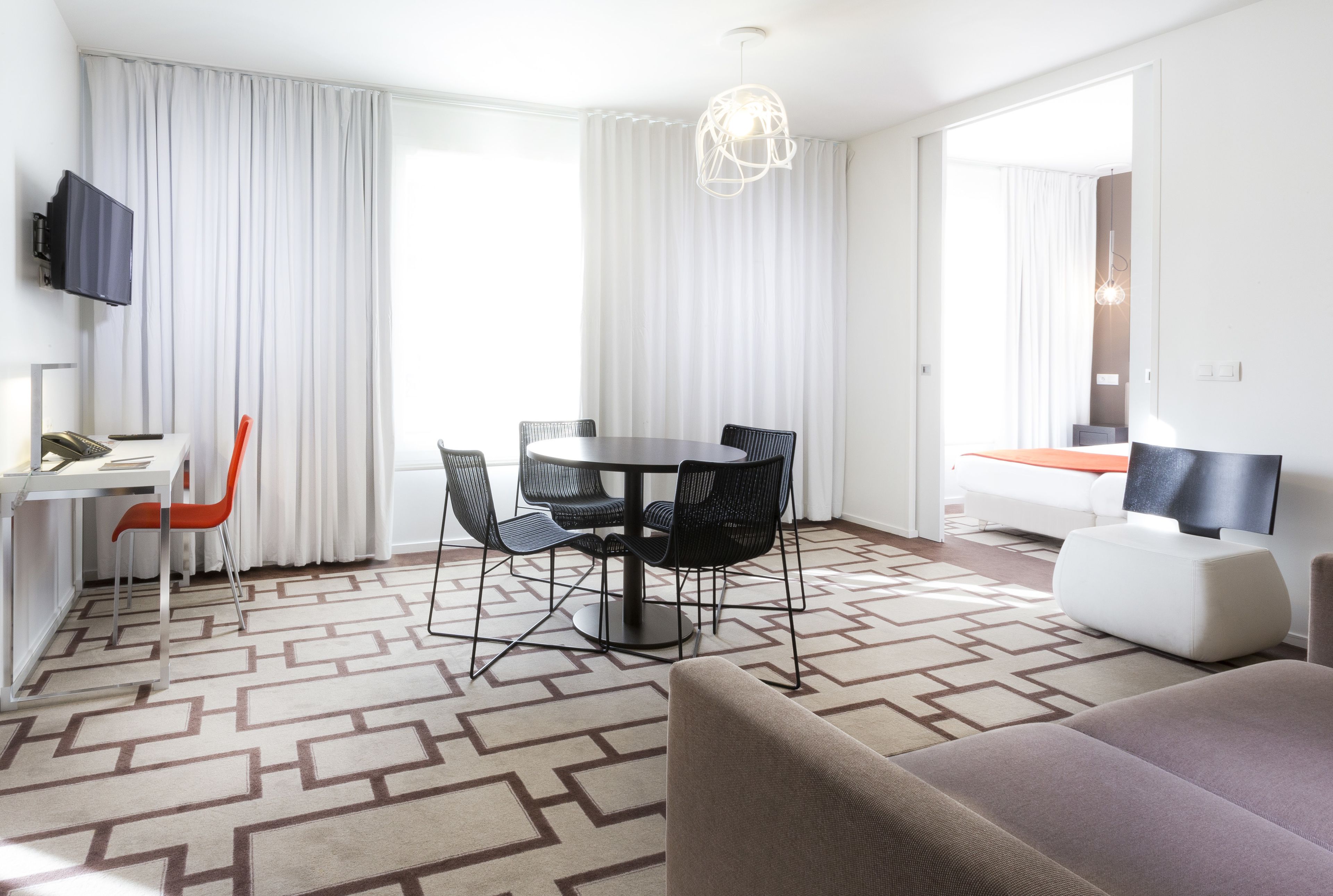 Una habitación de hotel moderna con zona de comedor, sofá y televisor.