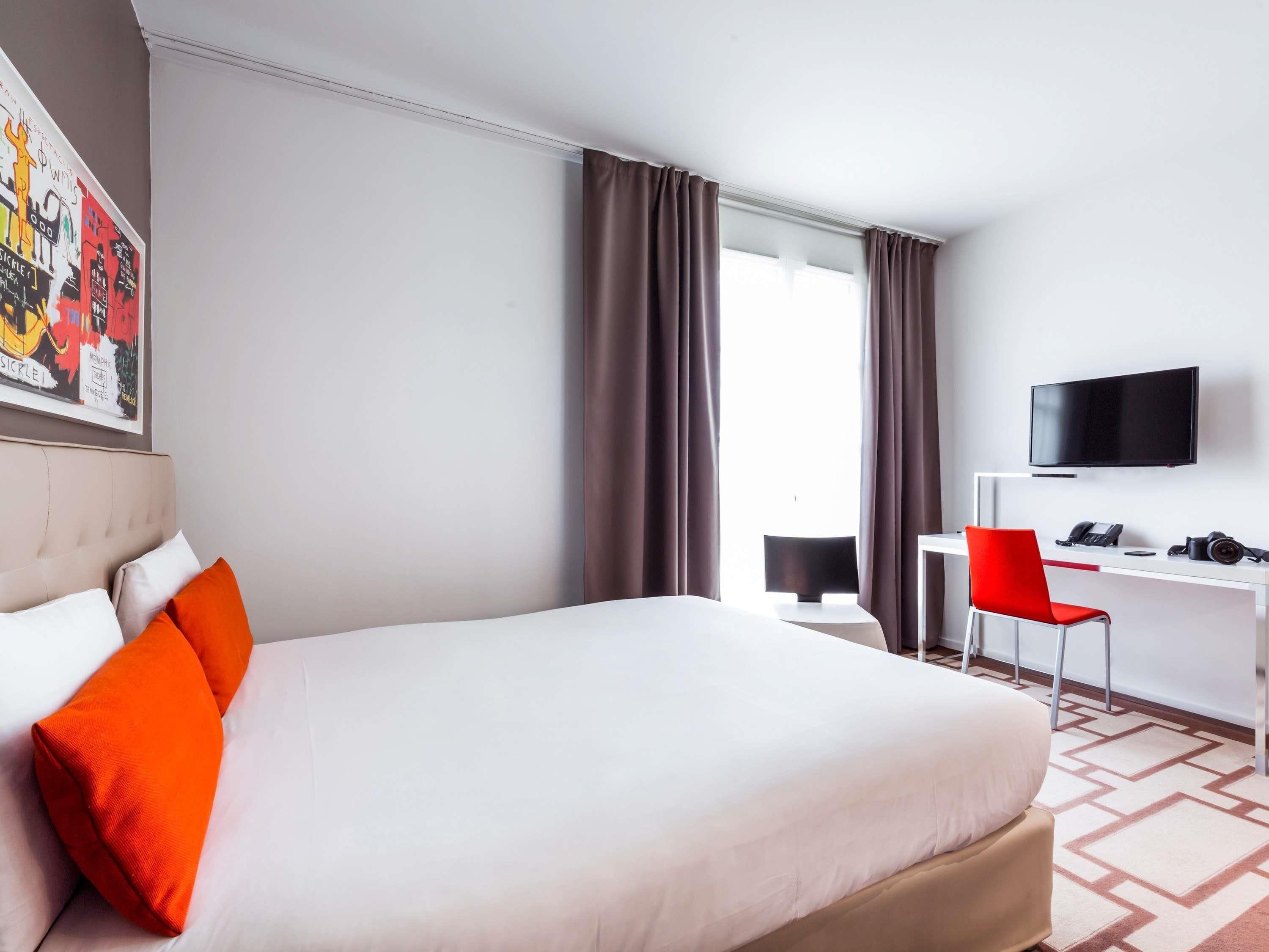 Ein Hotelzimmer mit Bett, Schreibtisch mit Stuhl, Fernseher und einem Fenster mit Vorhängen.