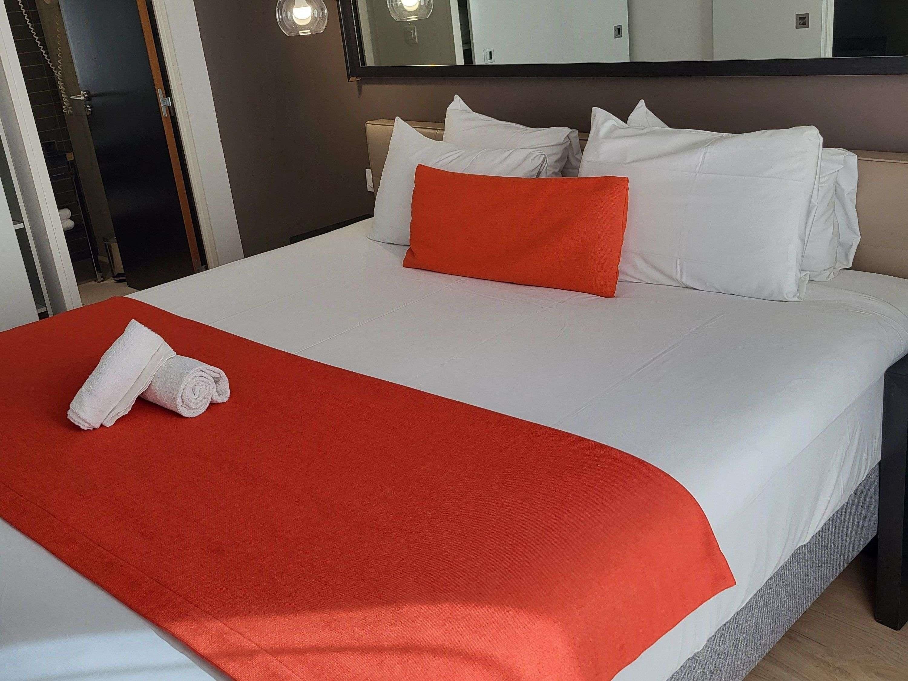 Una cama bien tendida con ropa blanca y una manta roja.