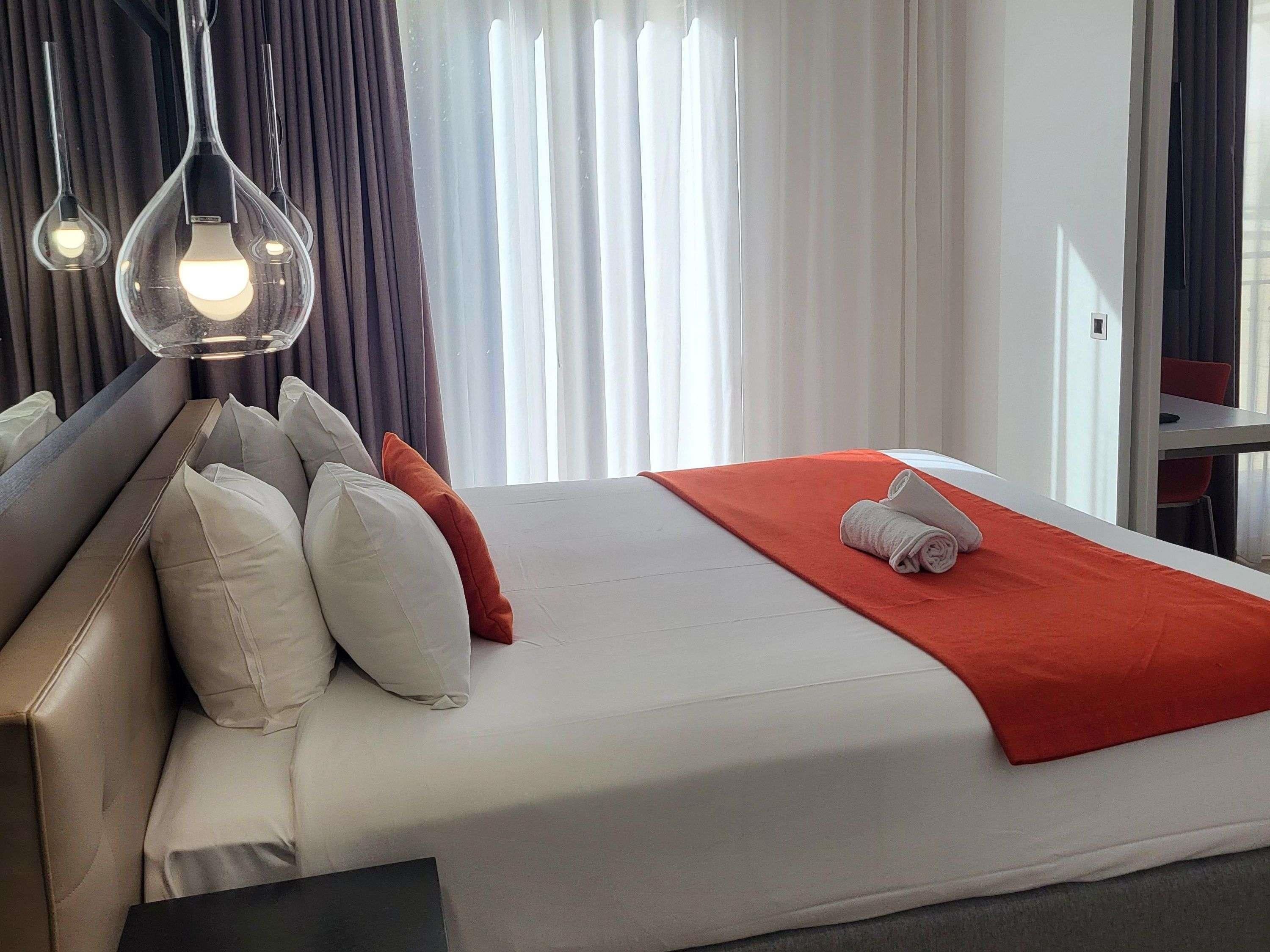 A hotel room with a bed, pillows, a red blanket, and a towel.