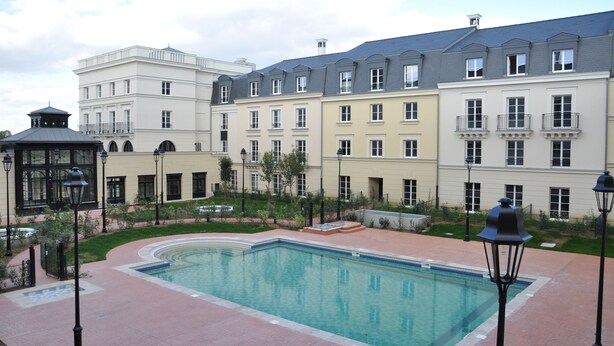 Une cour d’hôtel avec une piscine, un kiosque et une rangée d’immeubles à plusieurs étages.