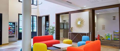 A modern lobby with colorful seating, a vending machine, and a large mirror on the wall.