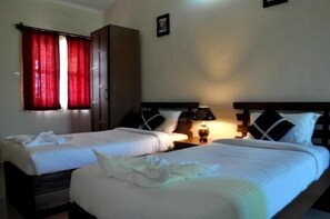 Habitación de hotel con dos camas, un armario, una mesita de noche con lámpara y una ventana con cortinas rojas.