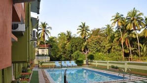 A swimming pool with a tiled deck, surrounded by palm trees and greenery. - A's Holiday Beach Resort (Betalbatim)