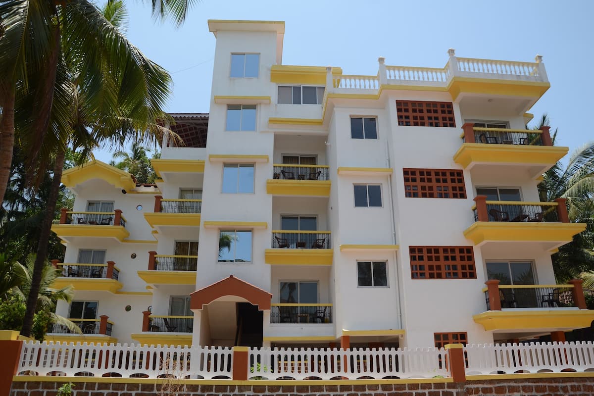 A multi-story building with balconies, a white and yellow color scheme, and a white picket fence in the foreground.
