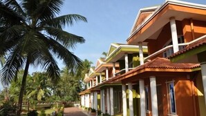 A row of hotel rooms with a central corridor, palm trees, and a clear sky. - A's Holiday Beach Resort (Betalbatim)