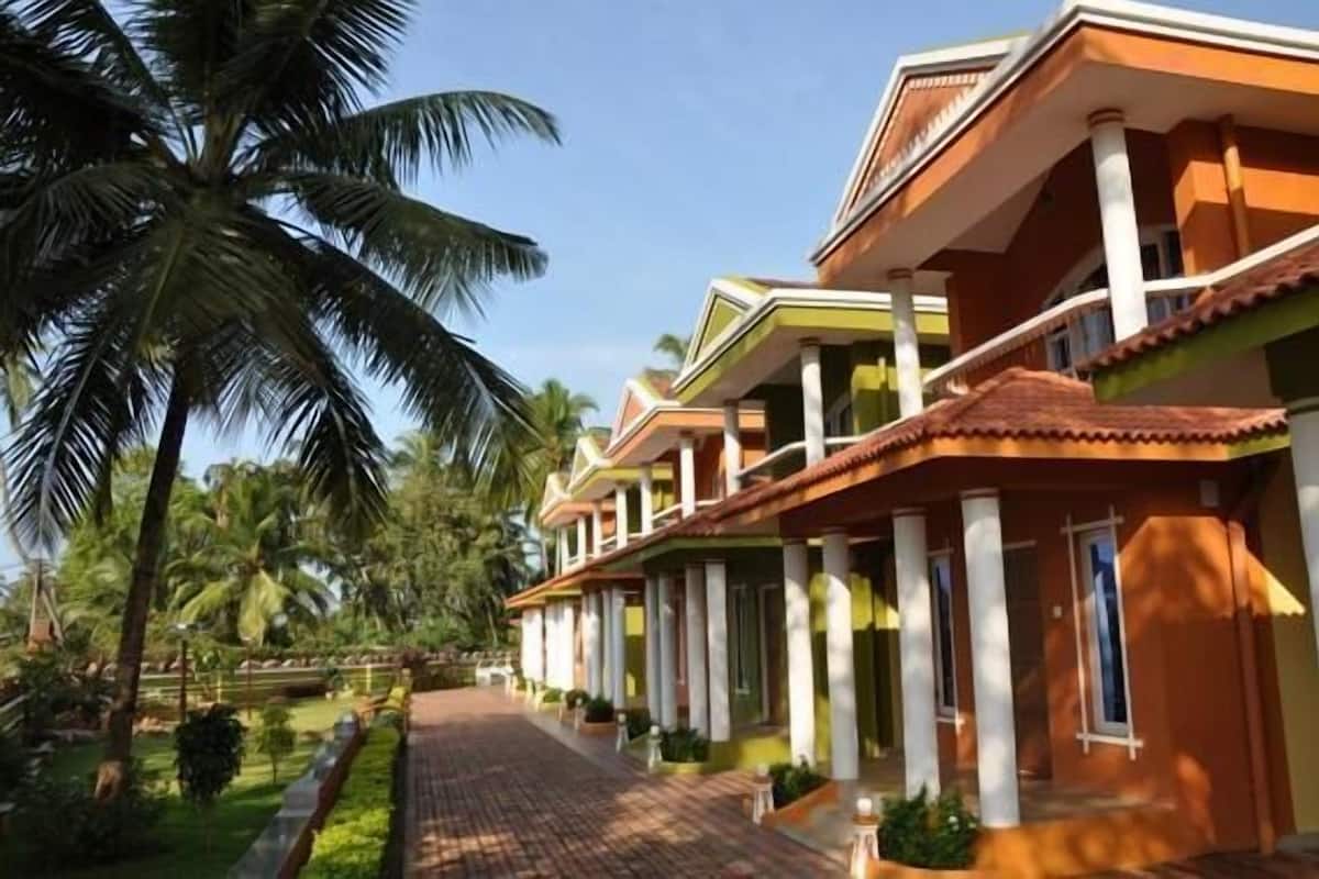 A row of hotel rooms with a central corridor, palm trees, and a clear sky.