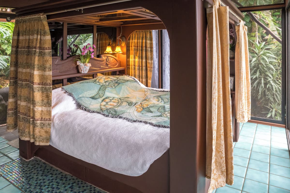 Een bed met een bloemenprint, een nachtkastje met een lamp en gordijnen.
