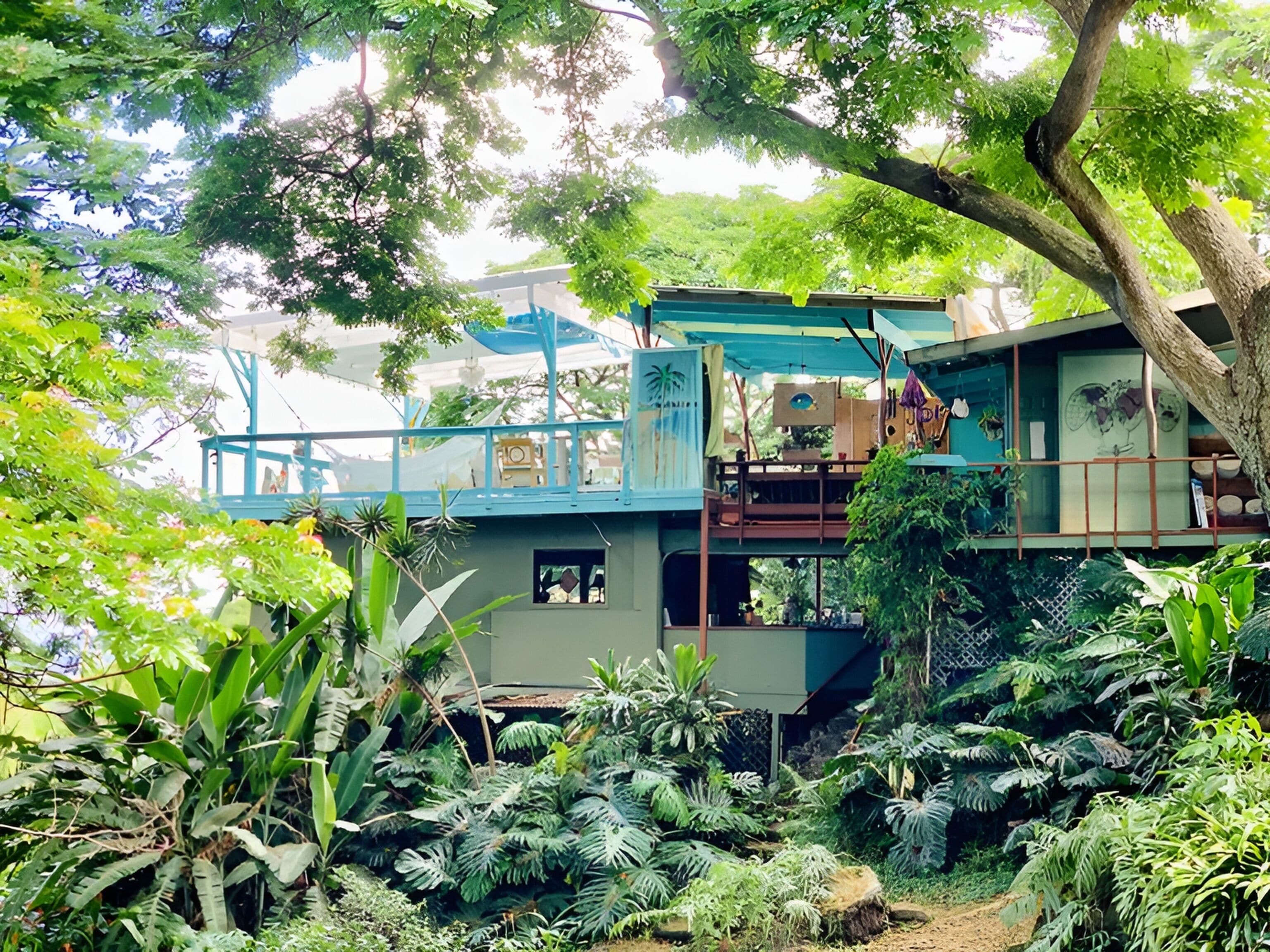 Una casa de dos pisos con un balcón, rodeada de exuberante vegetación y árboles.