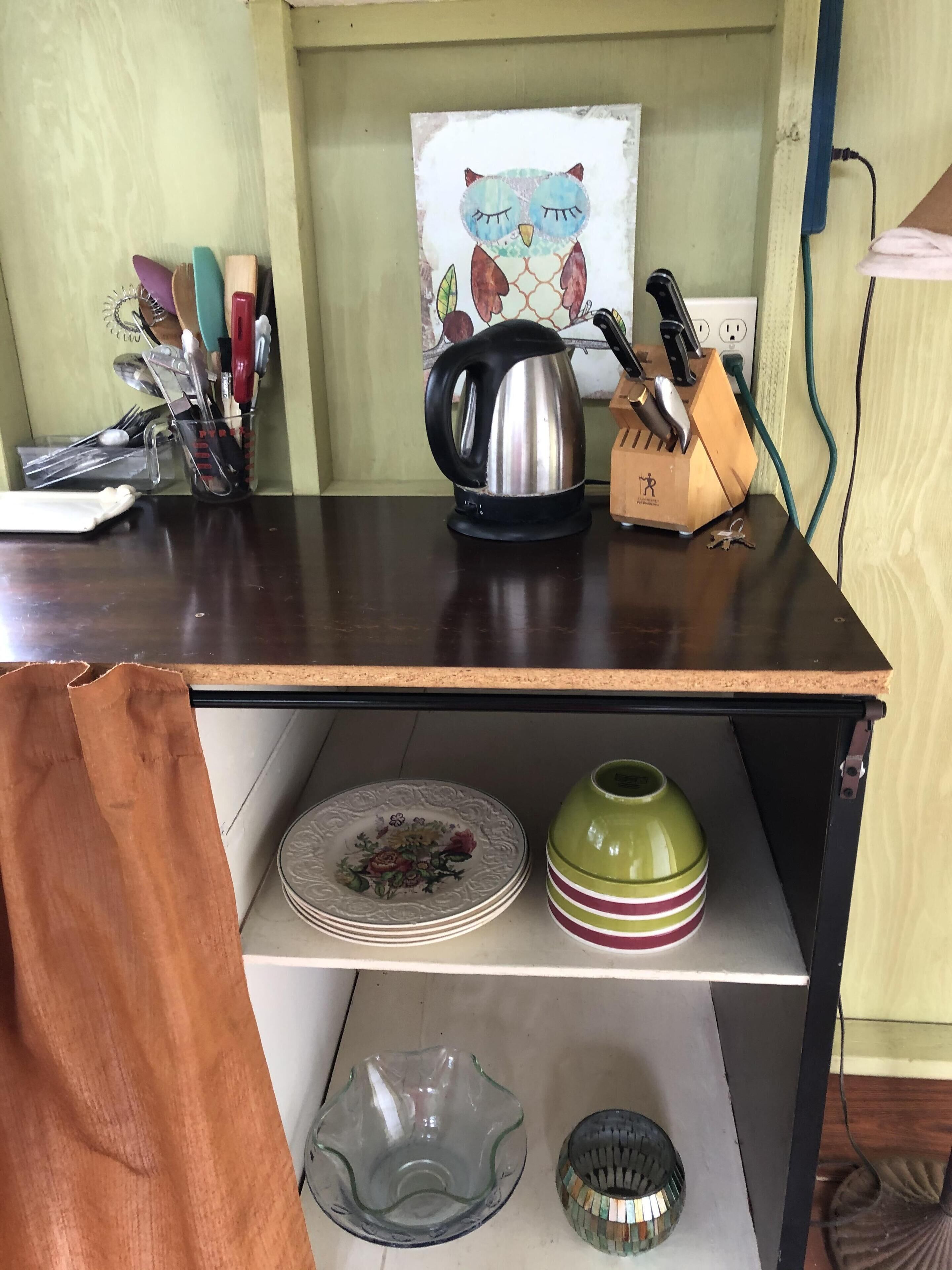 Una encimera de cocina con un hervidor, un bloque de cuchillos y un cuadro en la pared.