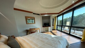 Un dormitorio con una cama grande, un escritorio de madera, una televisión y un amplio ventanal con vistas al exterior.