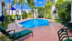 Una piscina rodeada de sillas verdes y abundante vegetación.