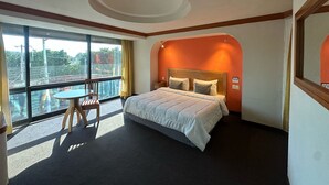 Habitación de hotel con una cama grande, una mesita y una silla cerca de una ventana que ofrece vistas al exterior.