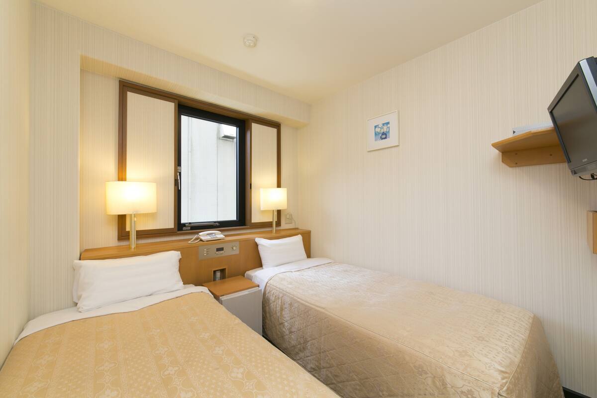 Une chambre d’hôtel avec deux lits, un téléviseur posé sur une étagère et une fenêtre donnant sur un beau paysage.
