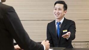 A man in a suit with a name tag at a reception desk, indicating a professional setting, likely a hotel or office. - Smile Hotel Shizuoka (Shizuoka)
