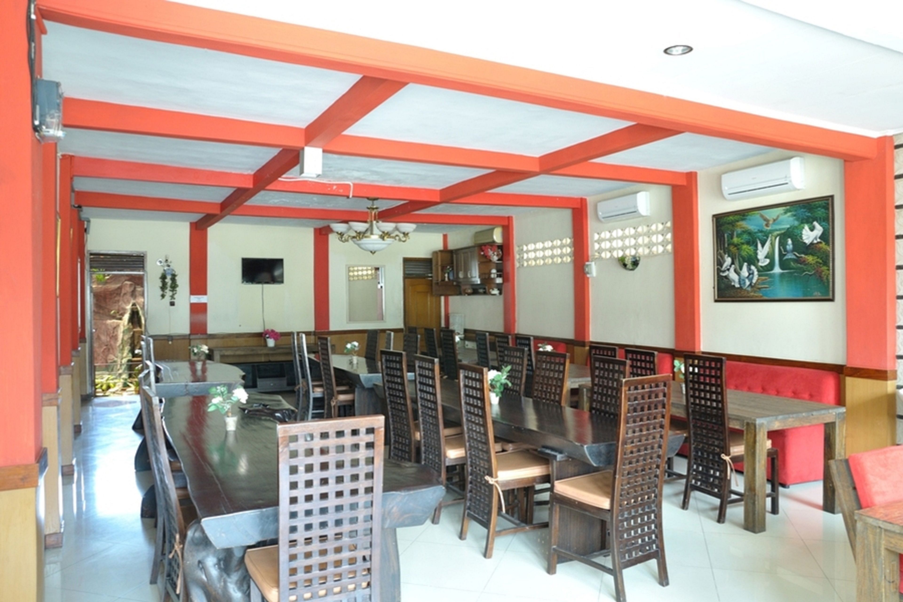 Un restaurante con mesas y sillas de madera, paredes rojas y blancas y un cuadro colgado en la pared.