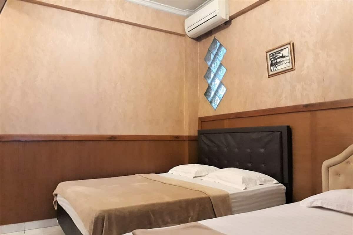 Hotellihuone, jossa on kaksi sänkyä, puupanelointi, seinälle asennettu ilmastointilaite ja kehystetty taulu.