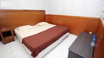 A single bed with a wooden headboard and a brown bedspread, a small wooden nightstand with a drawer, and a small table with a water bottle.