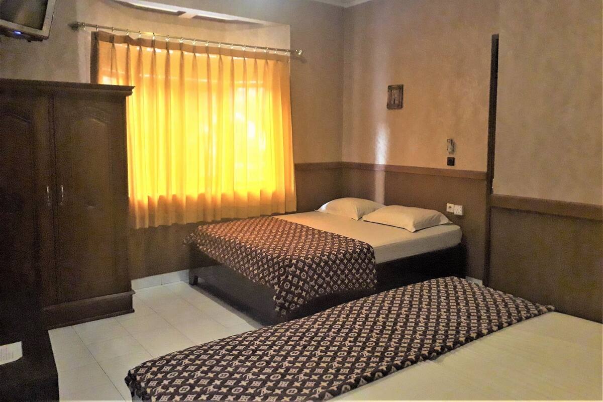 Hotellihuone, jossa on kaksi sänkyä, vaatekaappi, ikkuna verhoilla ja seinään asennettu valokytkin.