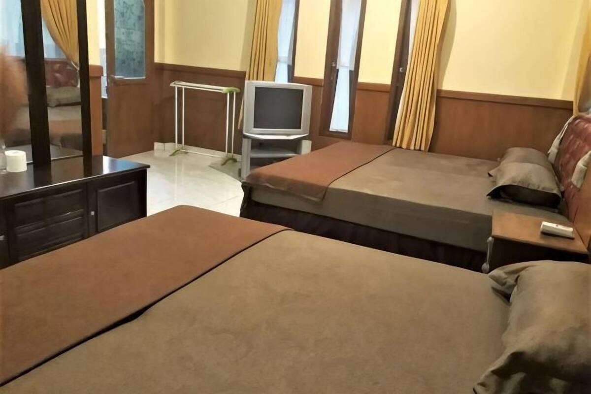 Hotellihuone, jossa on kaksi sänkyä, televisio, työpöytä ja peili.