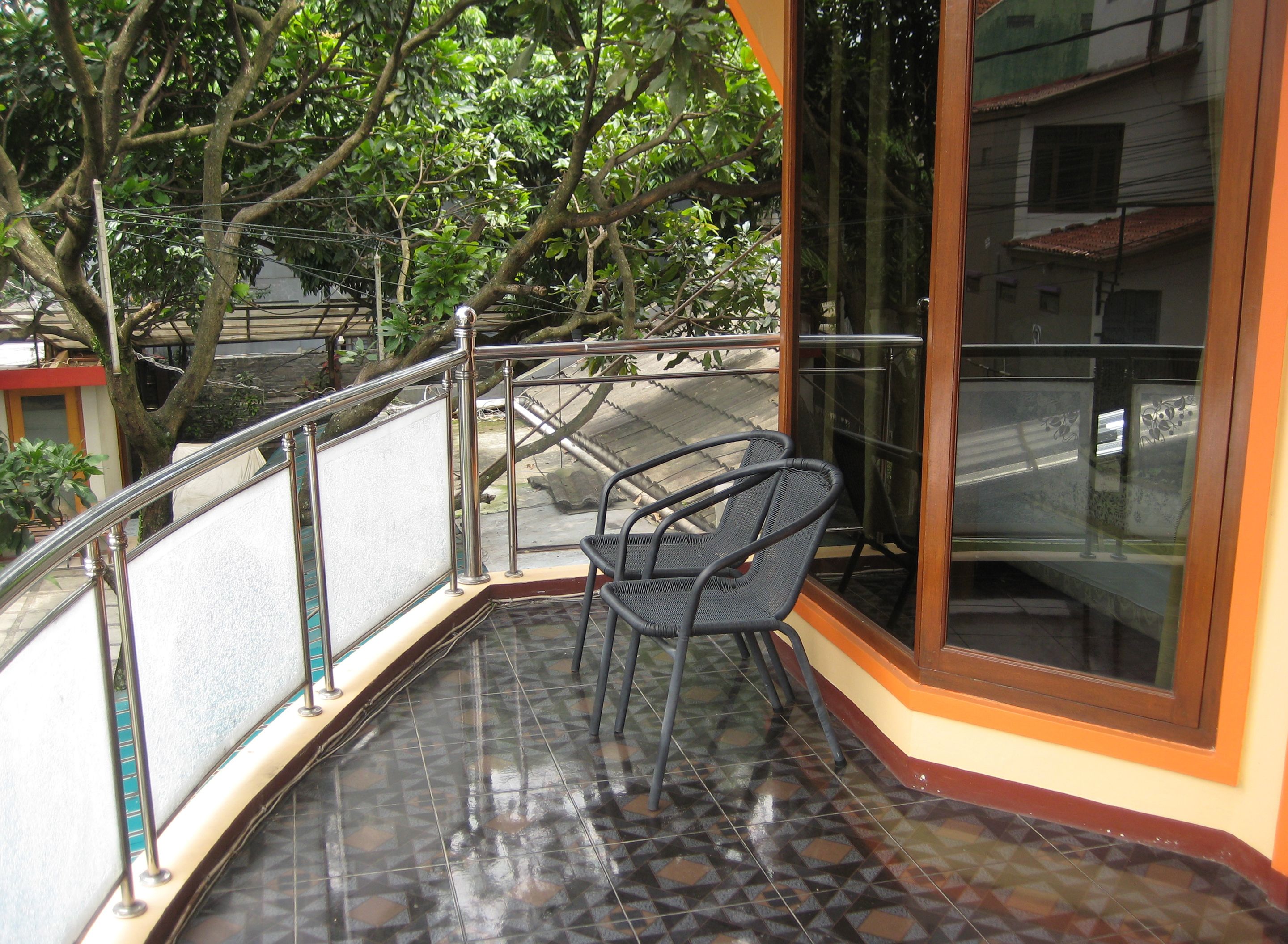 A balcony with a chair, metal railing, and a view of a street and trees.