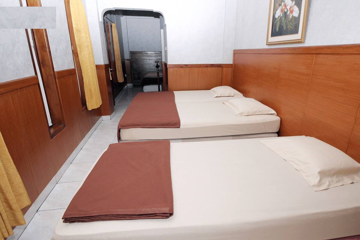 Hotellihuone, jossa on kaksi erillistä sänkyä, puiset päätyosat, pieni kylpyhuone, jossa on suihku, ja taulu seinällä.