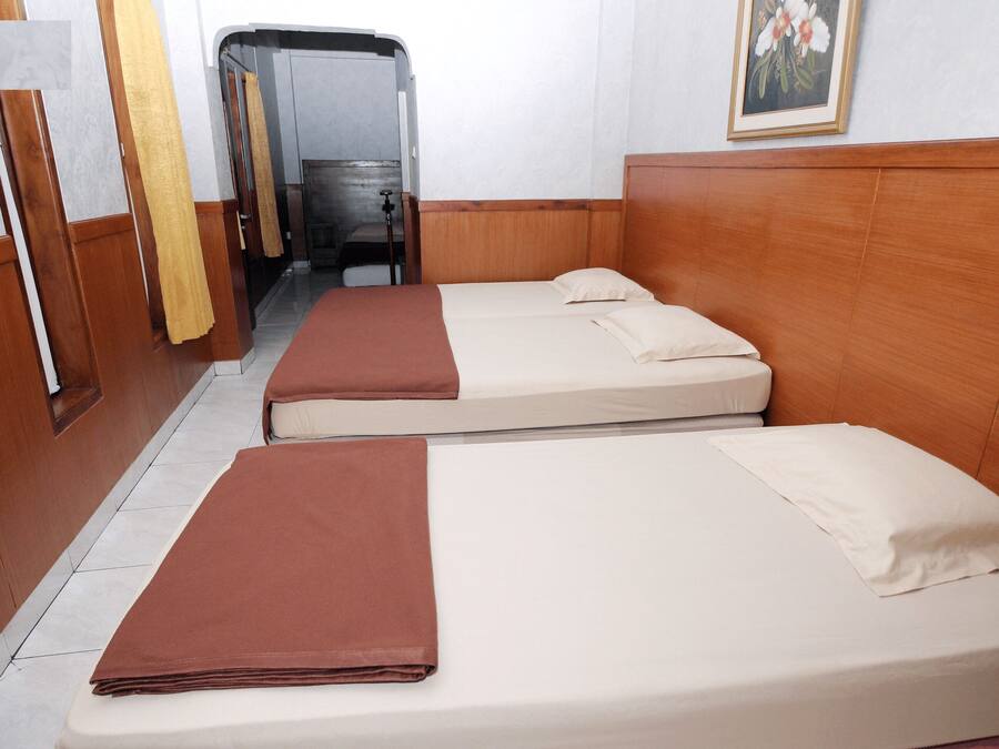 A hotel room with two single beds, wooden headboards, a small bathroom with a shower, and a painting on the wall.