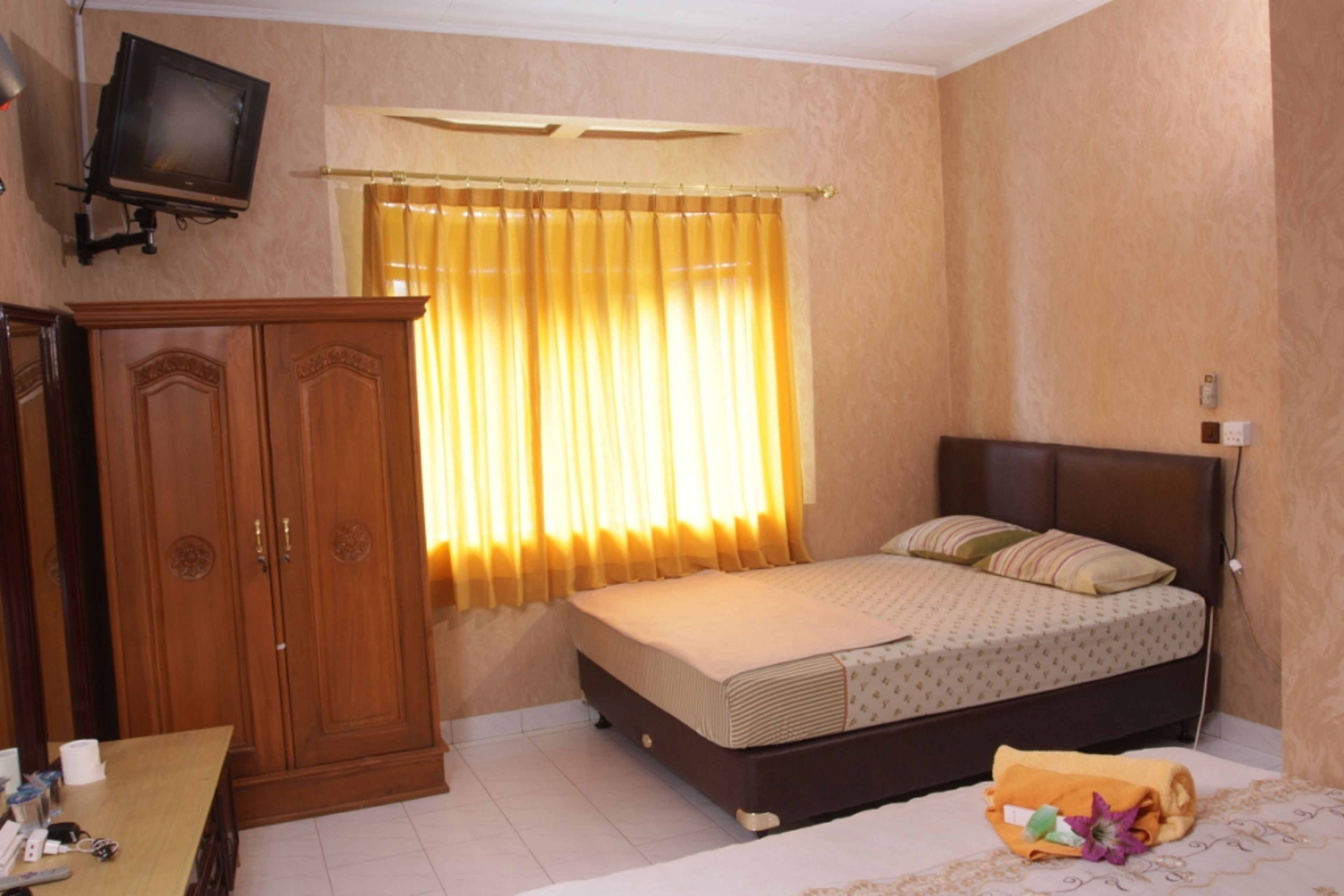 Quarto com cama, guarda-roupa, televisão e janela com cortinas.