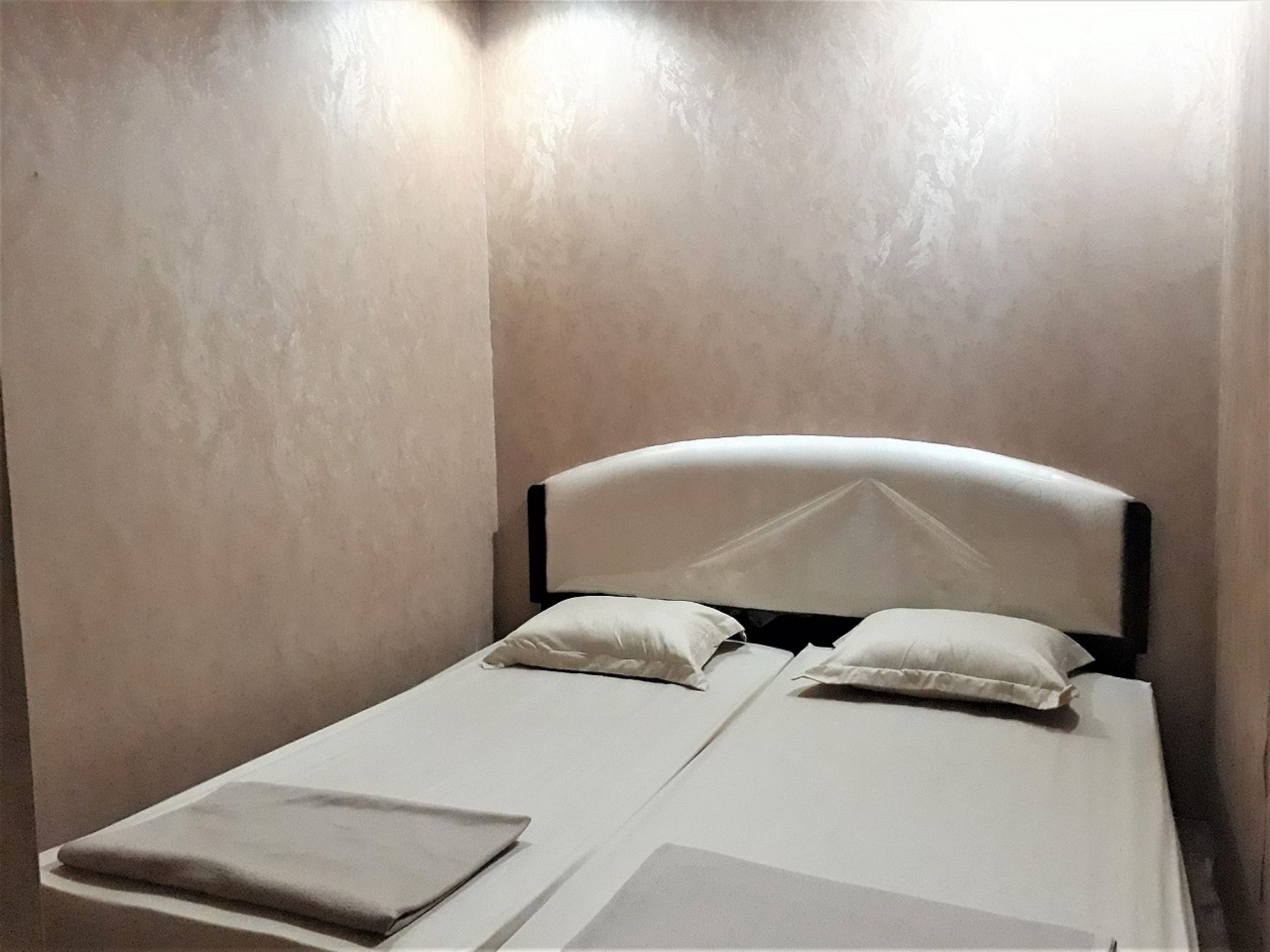 Una cama individual con cabecera, dos almohadas y un edredón doblado sobre una pared lisa.