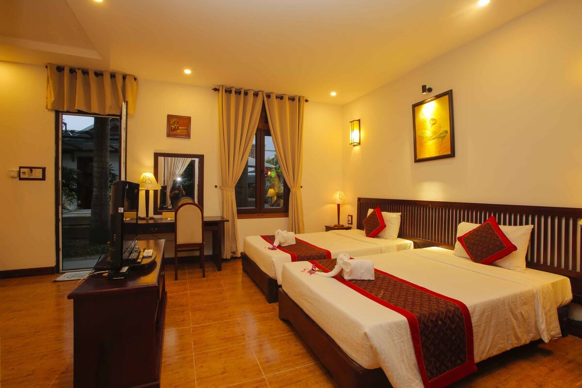 A hotel room with two beds, a desk, a chair, and a TV.
