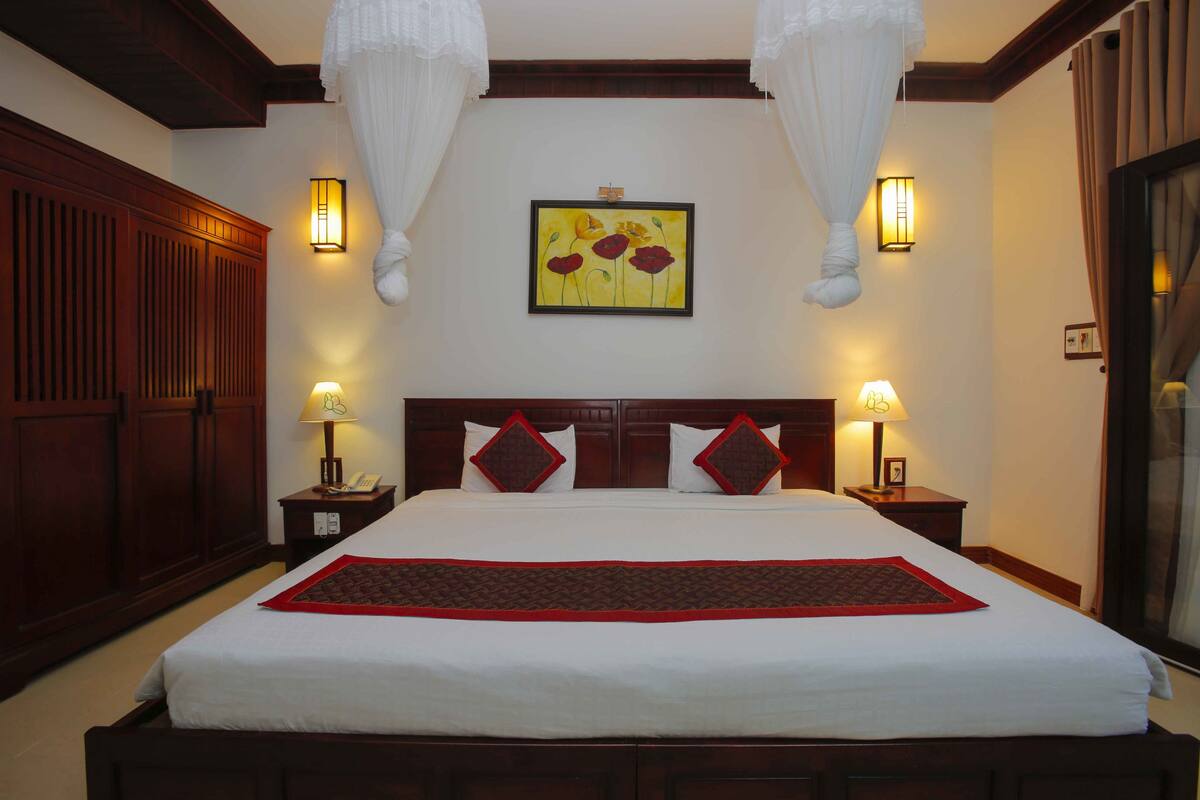 A hotel room with a large bed, wooden headboard, two bedside tables with lamps, and a wall-mounted painting.