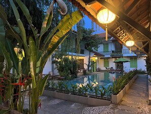 A pool area with a clear view of the surrounding architecture, including a two-story building with green shutters and a balcony. - Hoi An Garden Villas (Da Nang)
