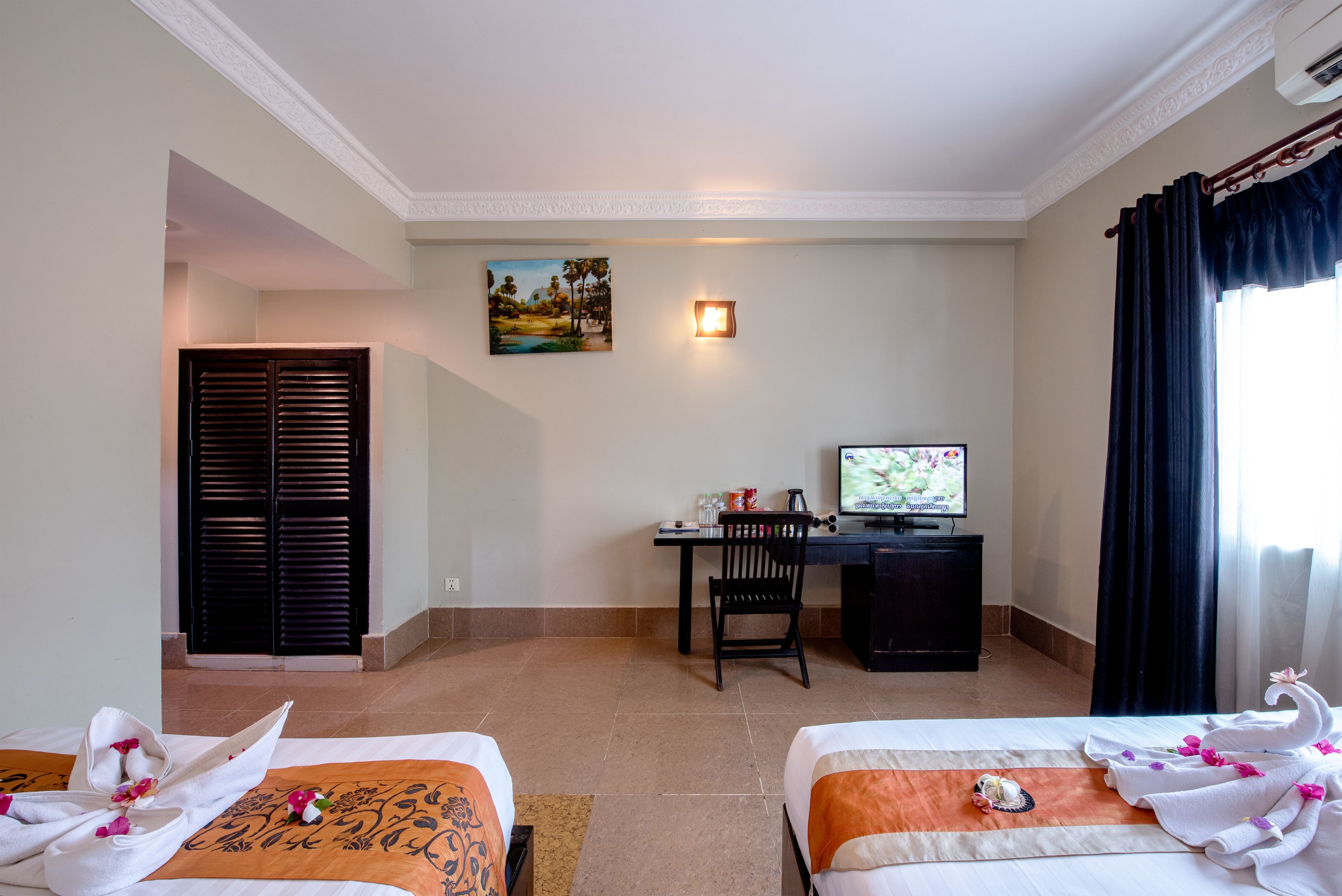 Une chambre d’hôtel avec deux lits, un bureau avec un ordinateur, un tableau au mur et une fenêtre avec des rideaux.