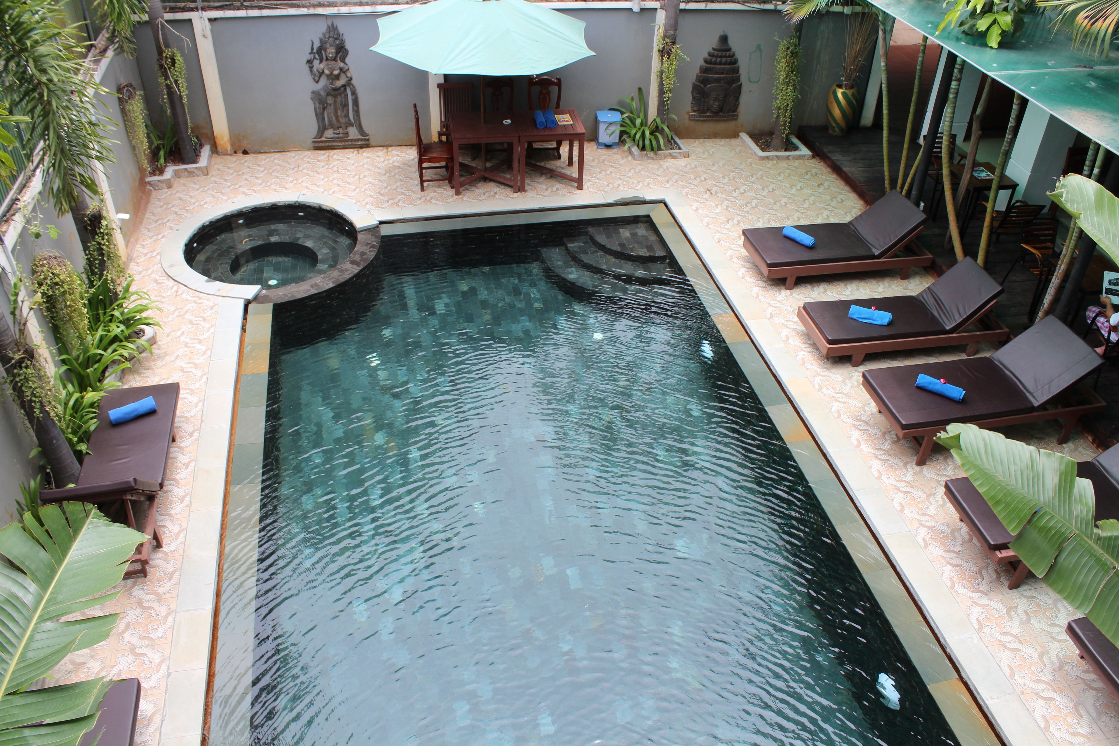 A swimming pool with lounge chairs and a table, surrounded by plants and a statue.