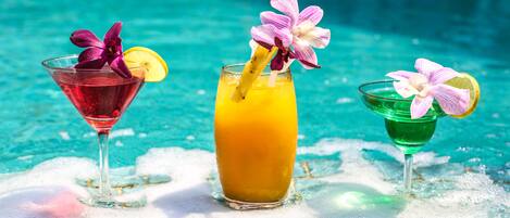 Three cocktails with flowers and fruit garnishes by a pool.