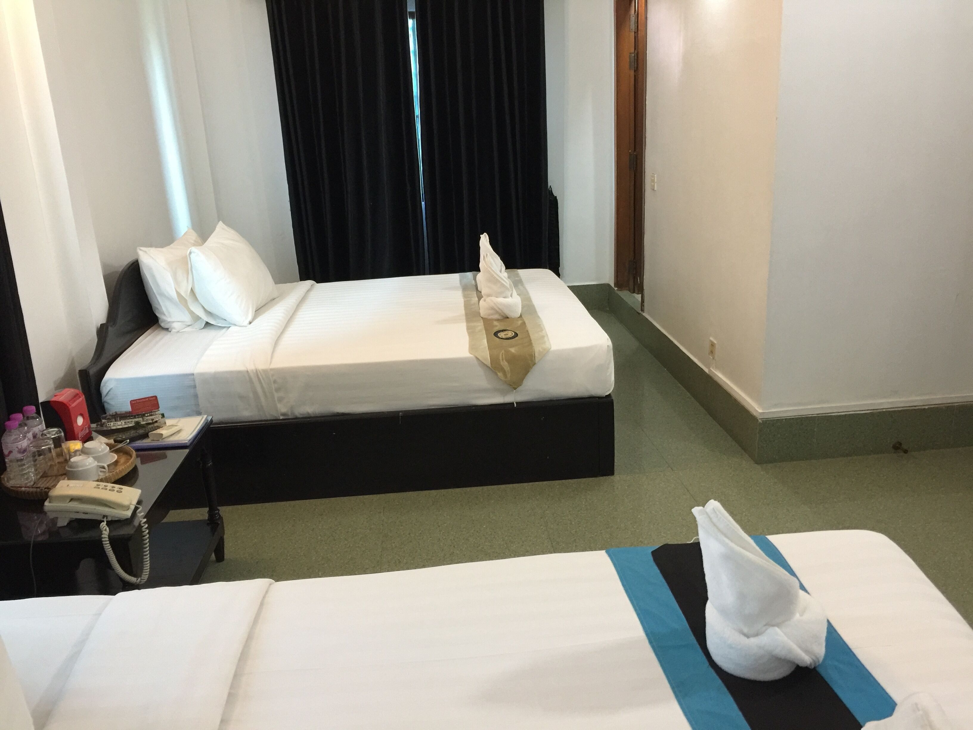 A hotel room with two beds, a bedside table with a phone, and a small table with toiletries.