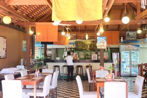 Ein Restaurant mit kariertem Boden, Holzbalkendecke, hängenden Lampen und einer Bar mit Hockern.