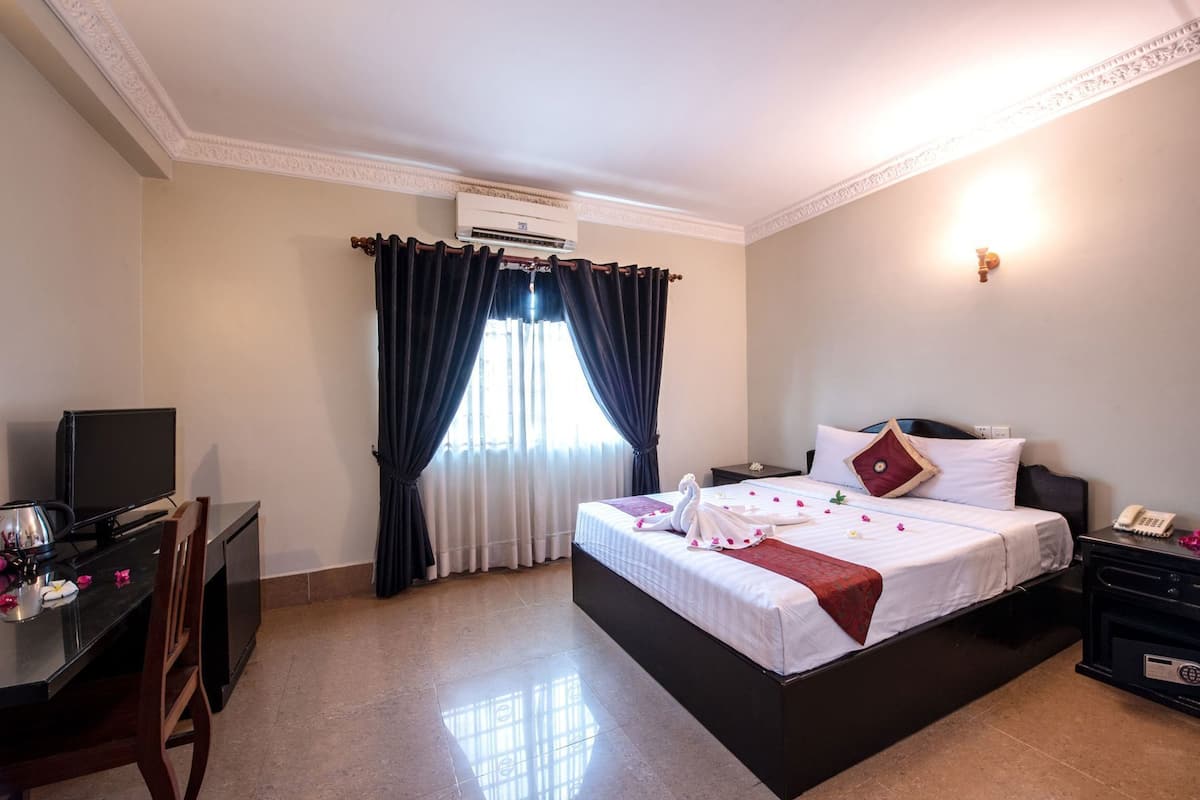 Une chambre d’hôtel équipée d’un lit, d’un bureau avec une télévision, d’un climatiseur et d’un téléphone.