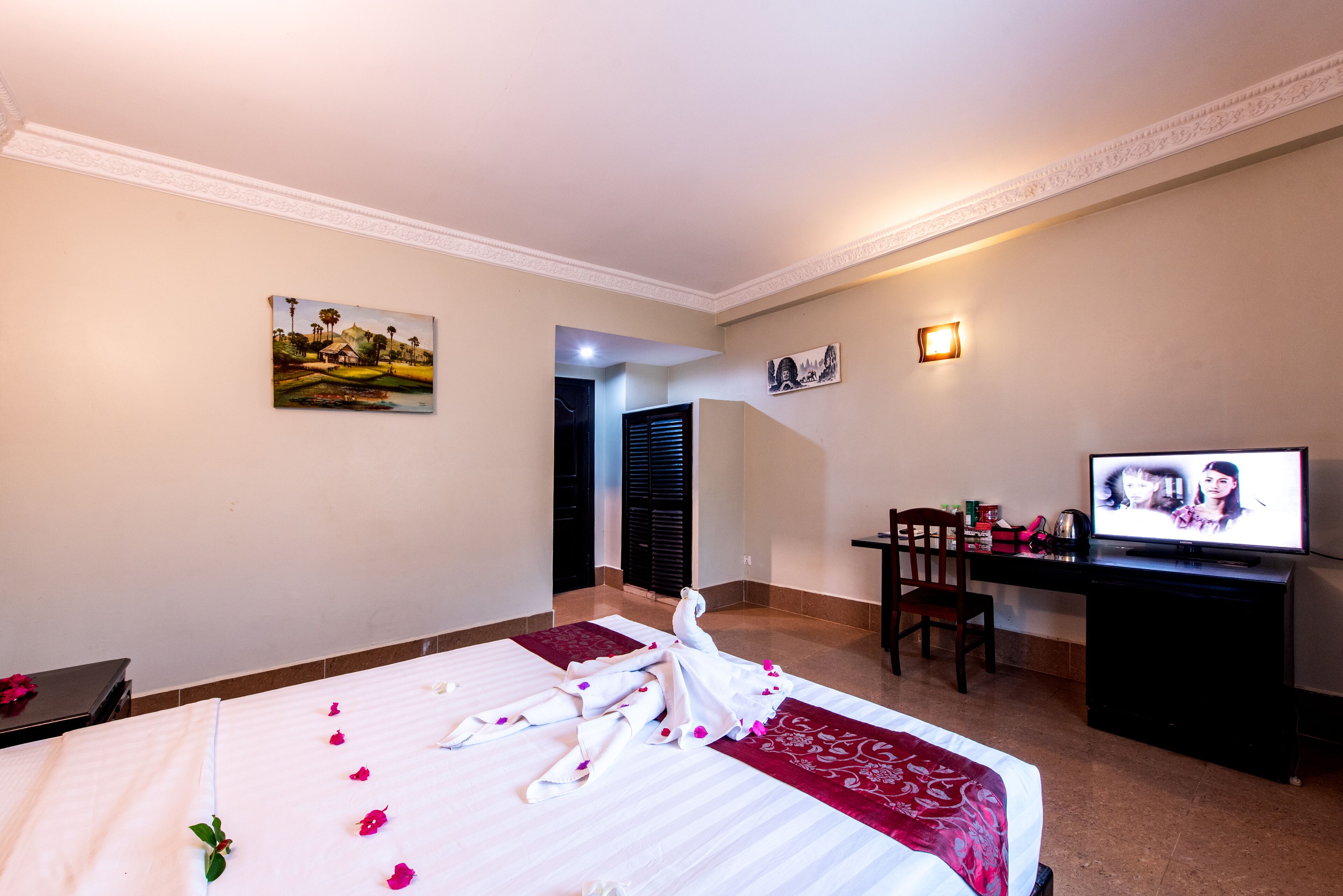 A hotel room with a bed, a desk, a television, and a painting on the wall.