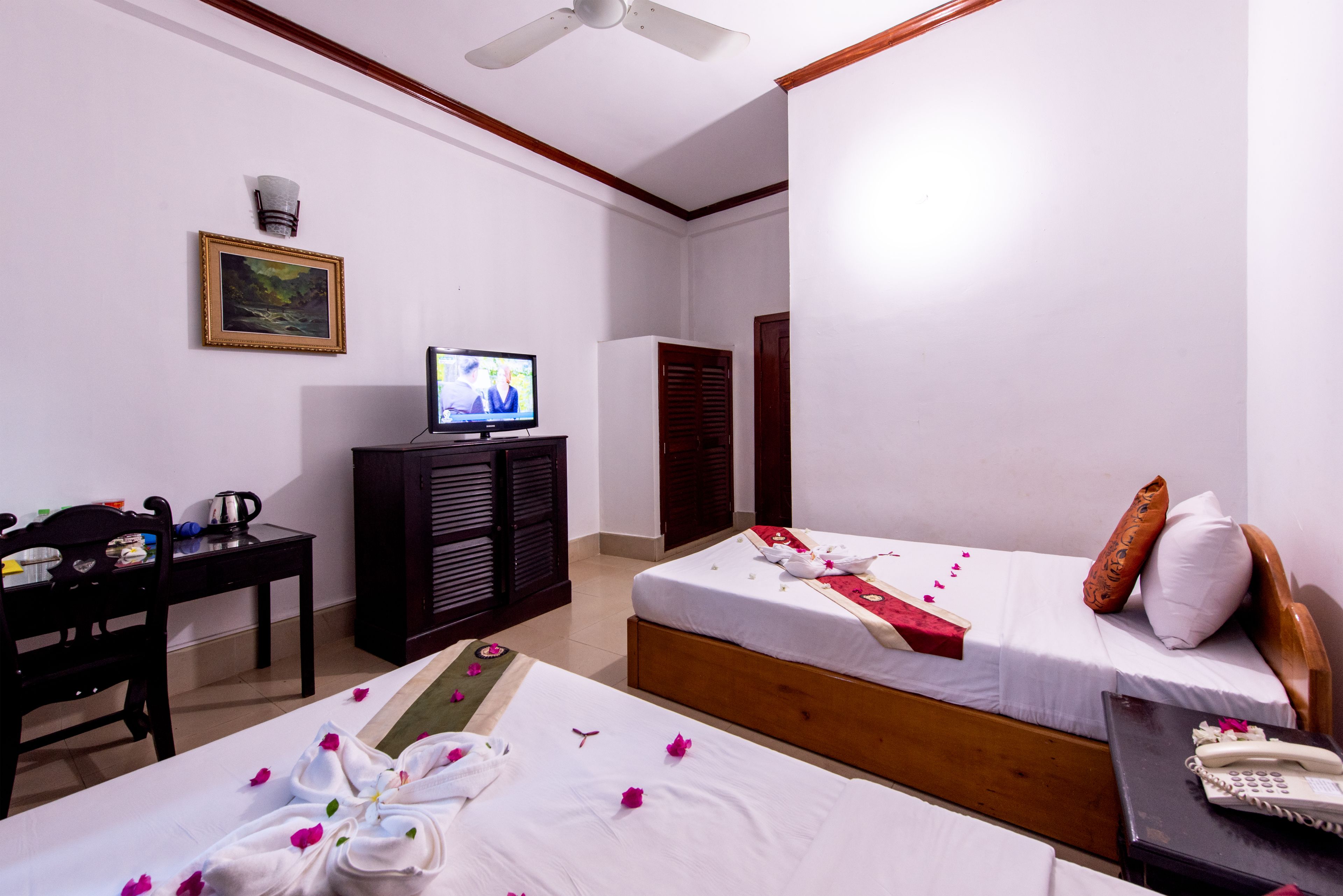 A hotel room with two beds, a television, a desk with a kettle, and a wardrobe.