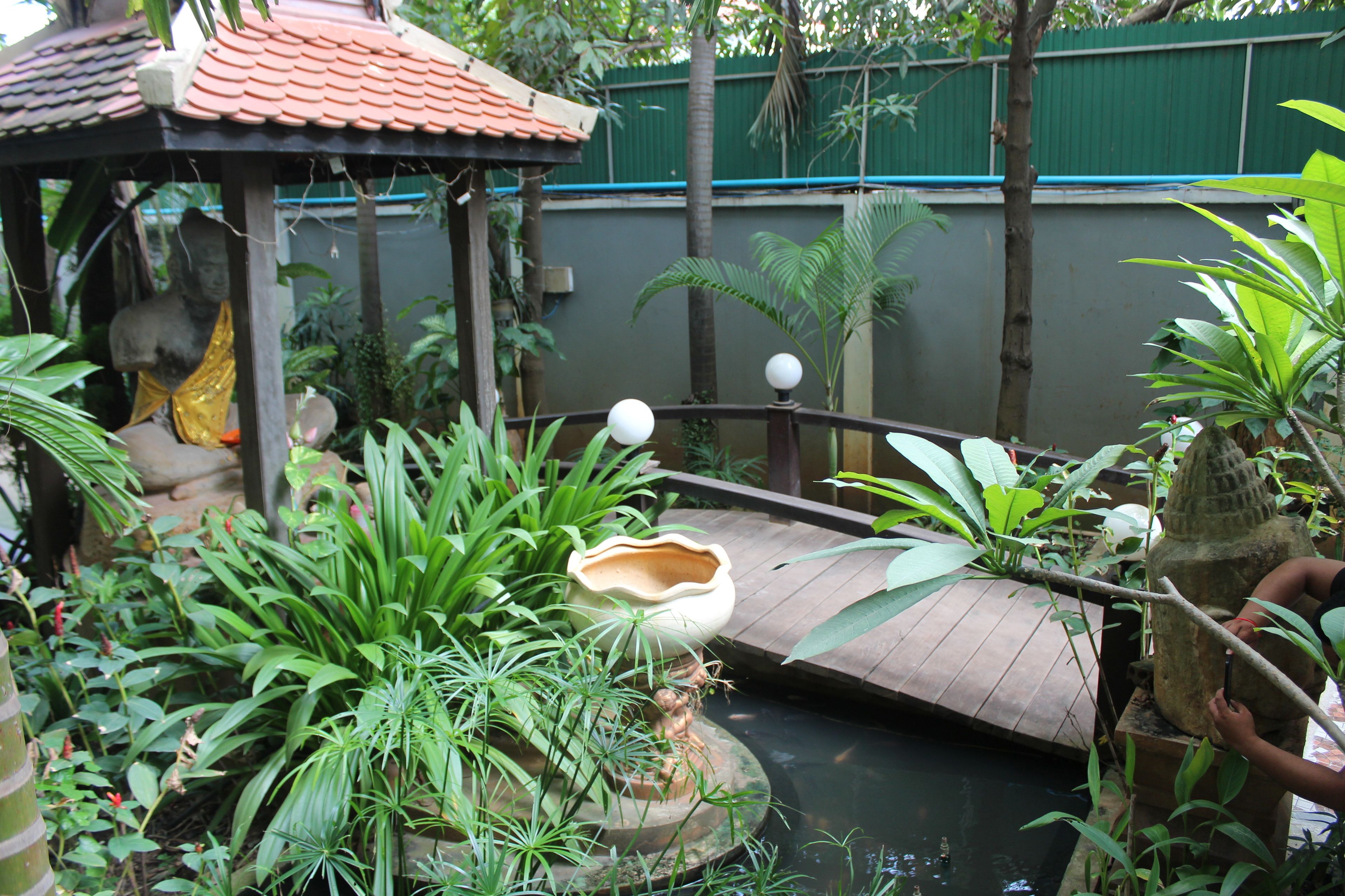 Un jardín con un estanque pequeño, un puente de madera y una estatua.