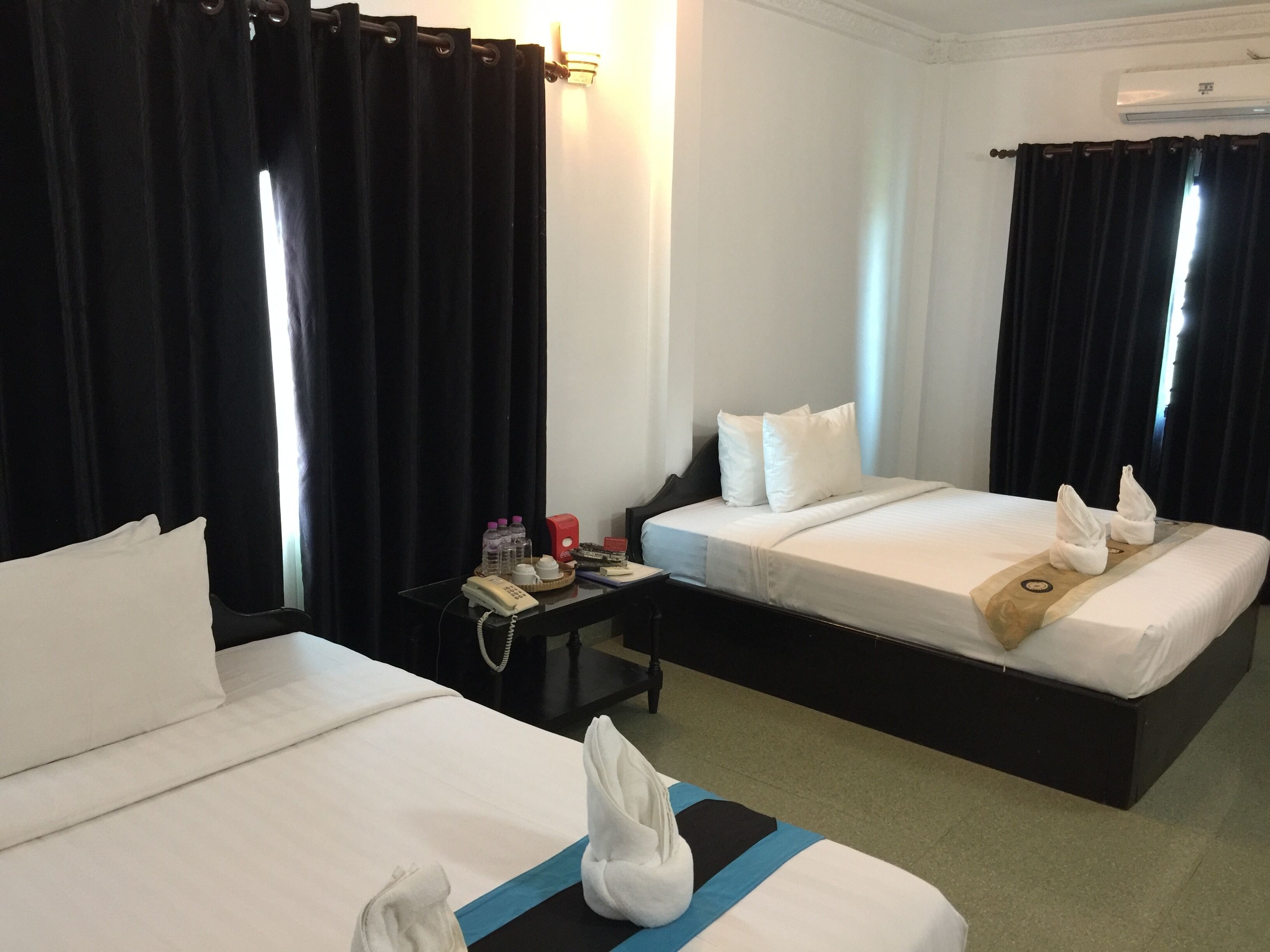 A hotel room with two beds, a bedside table with a phone and toiletries, and a wall-mounted air conditioner.