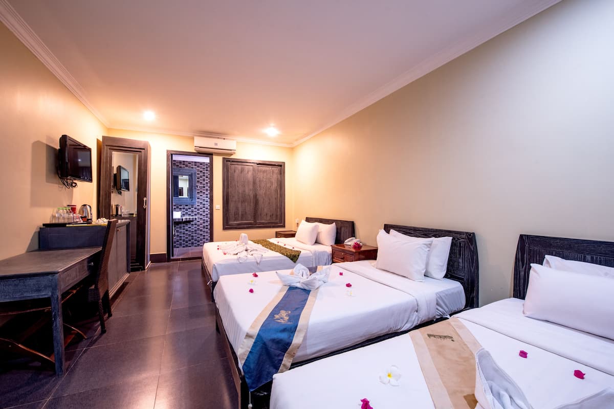 Une chambre d’hôtel avec trois lits, un bureau et une télévision.