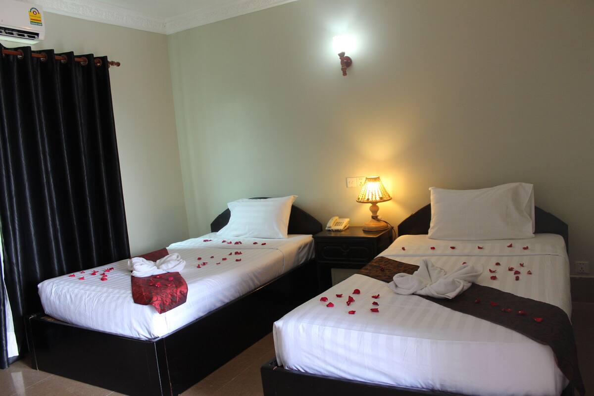 Une chambre d’hôtel avec deux lits simples, une table de chevet avec une lampe et un téléphone fixé au mur.
