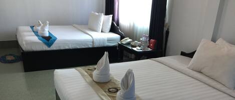 Hotelkamer met twee bedden, elk voorzien van witte lakens en handdoeken. Er is een nachtkastje met een telefoon, een rood beker en een fles. De kamer heeft een raam met gordijnen en uitzicht op buiten.