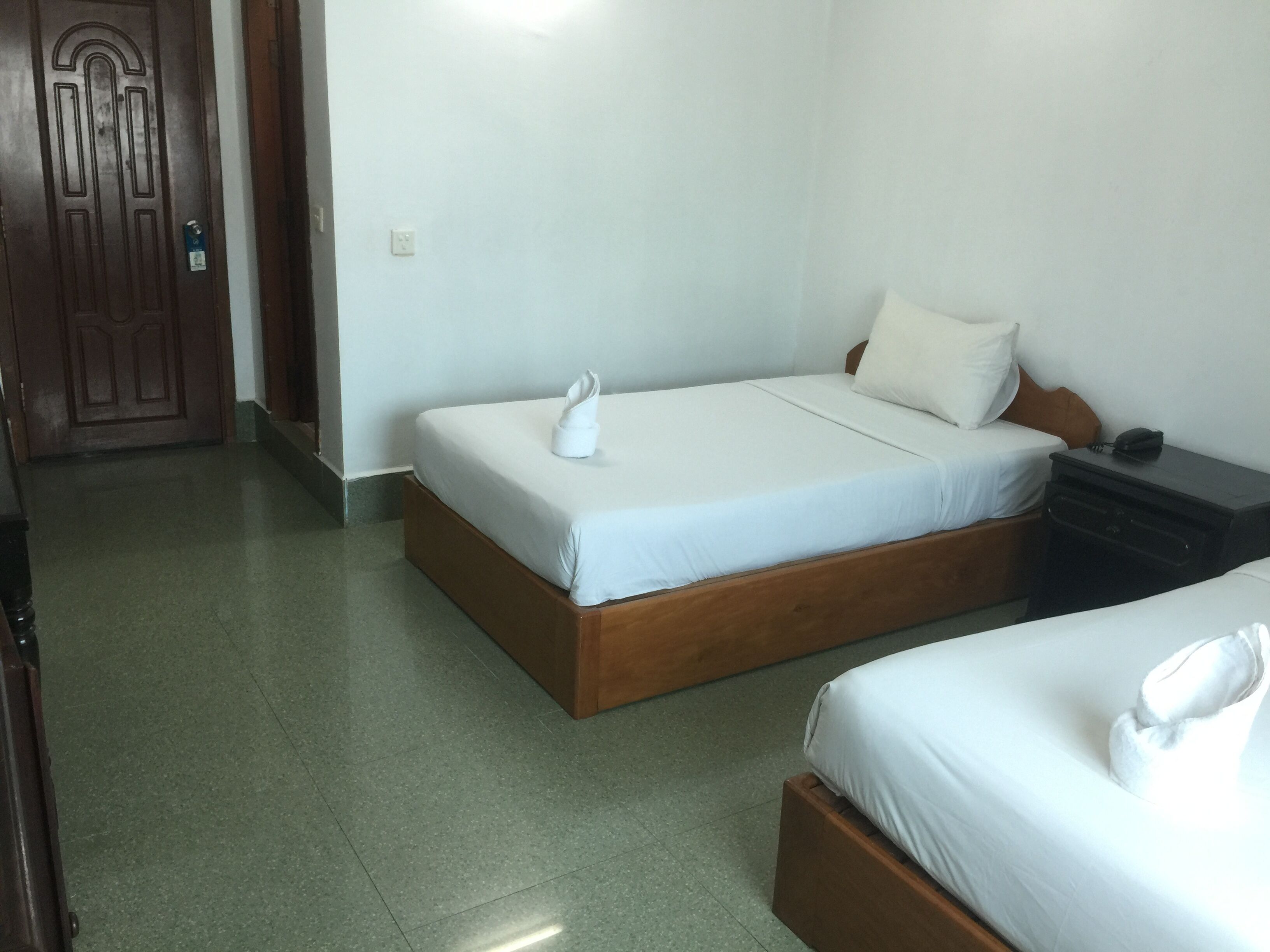 A hotel room with two beds, a wooden door, a nightstand, and a telephone.