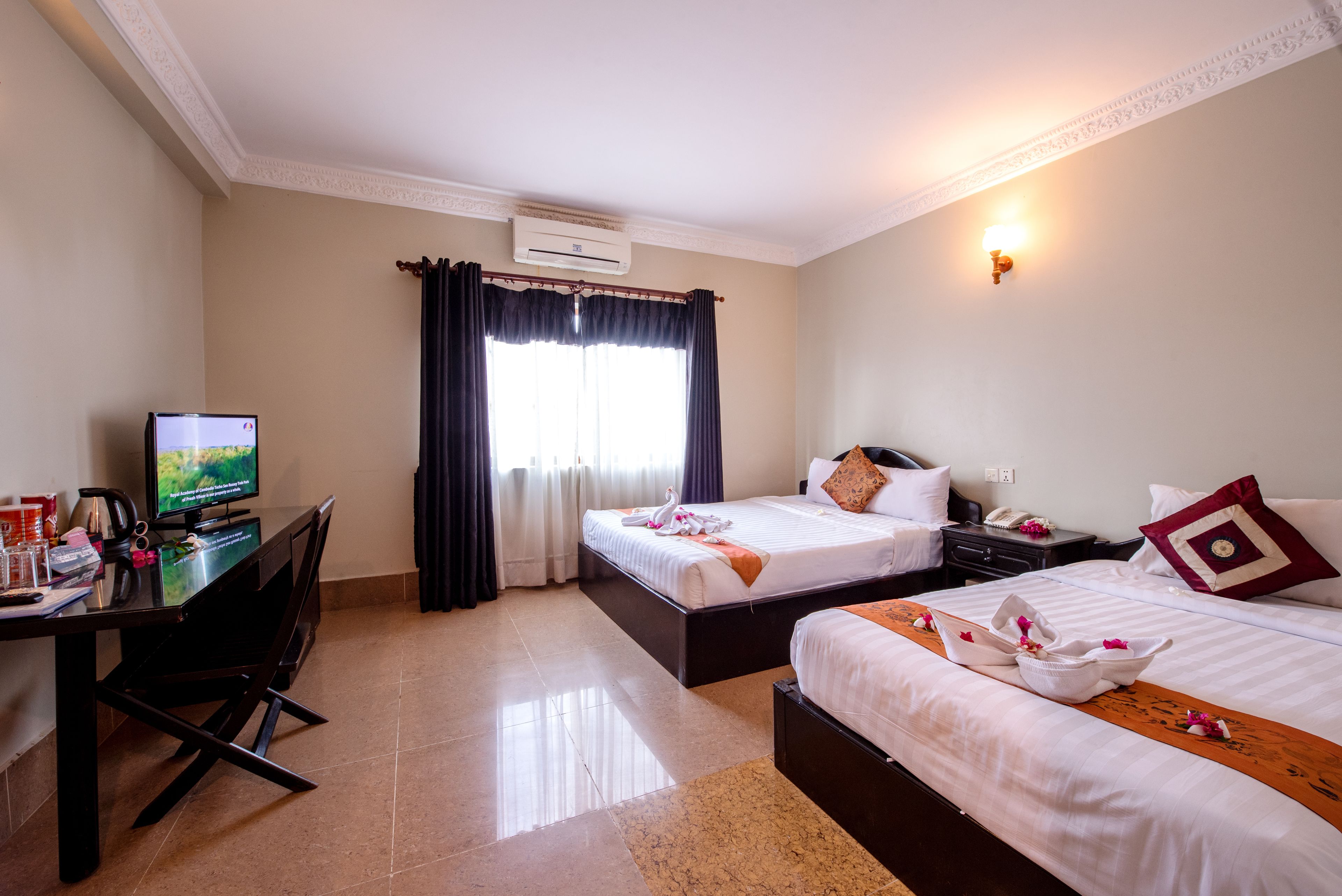 A hotel room with two beds, a desk with a computer, and a window with curtains.