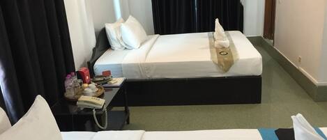 A hotel room with a bed, a bedside table with a phone, a tray with toiletries, and a window with curtains.