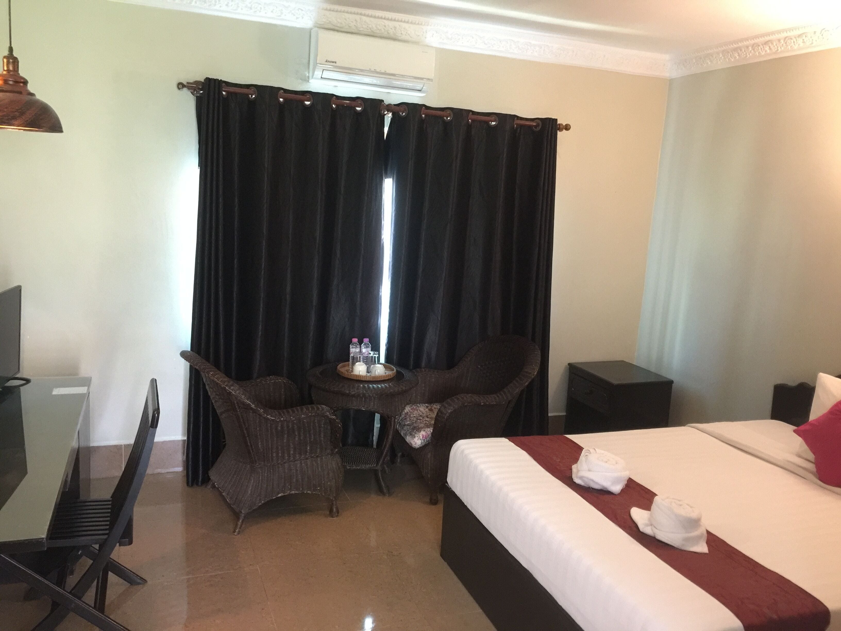 Habitación de hotel con cama, escritorio, dos sillas, una mesita con bandeja de artículos de aseo y una mesita de noche.